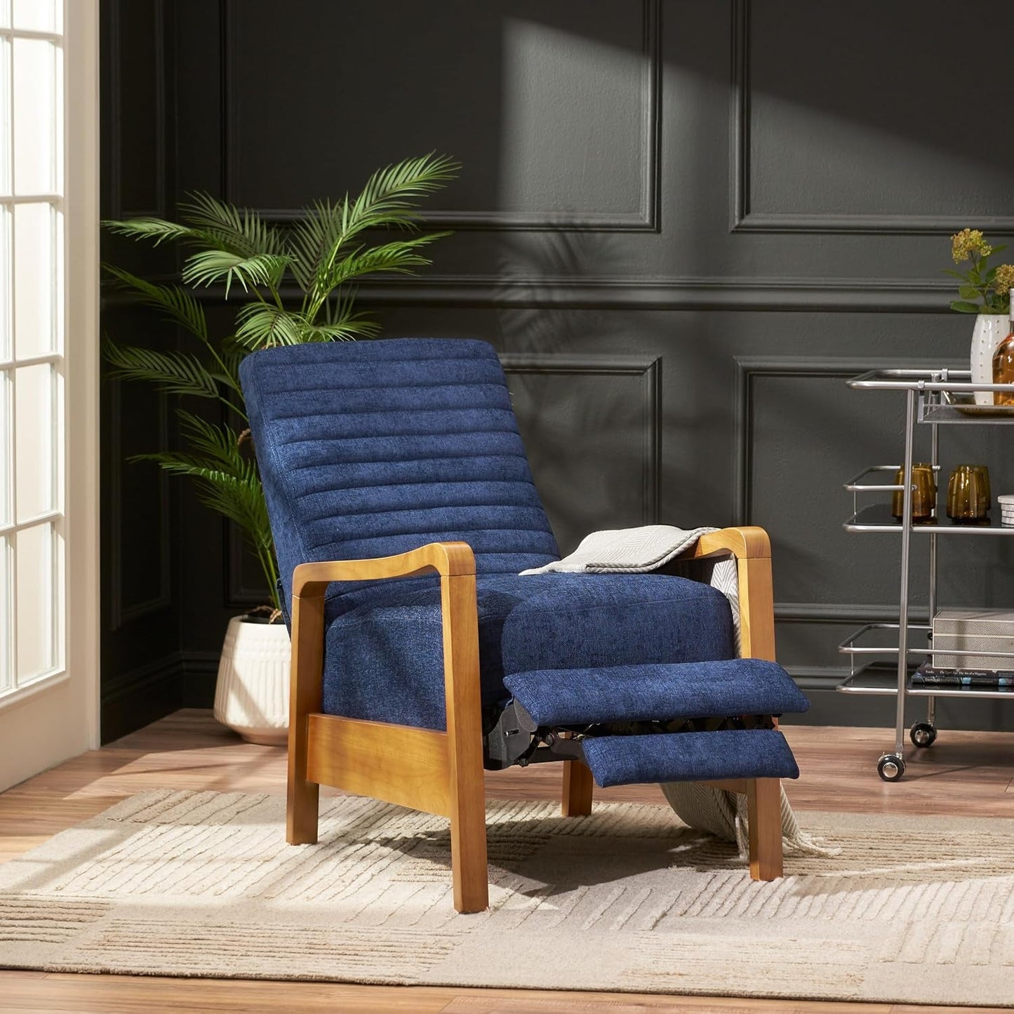 A mid-century modern recliner chair in navy blue fabric with the footrest extended, showcasing the full reclining function and a comfortable position for relaxation. The chair features a light wood frame.